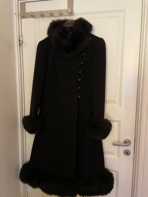 Svart kappa med pälsdetaljer Mark Stevens - Säljer en fantastisk och ovanlig svart 70-talskappa från märket Mark Stevens med fluffiga pälsdetaljer vid krage, ärmslut och nederkant. Kappan har en elegant, lång siluett och dekorativa knappar framtill. Använt fåtal gånger i mycket bra skick. Ingen storlek uppgiven, uppskattas till S. Prisförslag välkomna, skriv ditt bud i chatten