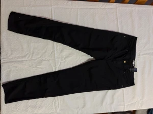 Svarta skinny jeans från H&M, stl 42 - Svarta skinny jeans från H&M i storlek 42. Klassisk femficksmodell med smal passform och normal midja. Byxorna har dragkedjegylf och bälteshällor, perfekta till sneakers eller boots. Materialet är mjukt och stretchigt för extra komfort.