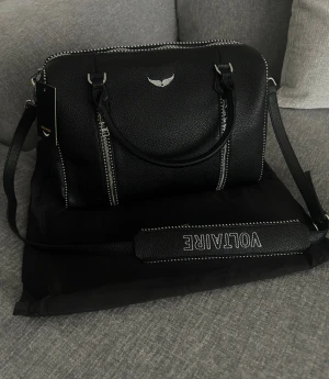 Svart axelväska från Zadig&Voltaire - Snygg svart axelväska från Zadig& Voltaire med silverfärgade detaljer och dragkedjor. Väskan har både handtag och justerbar axelrem med broderad logga. Tillverkad i skinn med strukturerad yta och coola kontrastsömmar. Priset kan diskuteras vid snabb affär! 