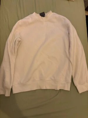 Vit sweatshirt från H&M relaxed fit - Vit sweatshirt från H&M i relaxed fit med ribbad krage, ärmslut och nederkant. Diskret broderad text på bröstet. Mjuk insida och klassisk rund hals. Perfekt för chill dagar och enkel att matcha med jeans eller joggers.