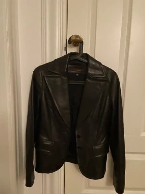 Adriano Goldschmied svart  skinnkavaj med klassisk krage - Snygg svart kavaj i skinn med klassisk krage och två knappar framtill. Jackan har två fickor och är helsvart med stilren design. Perfekt för dig som vill ha en edgy och tidlös look. Långärmad och med en normal passform.