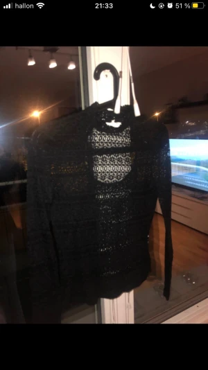 Svart spetsblus med lång ärm - Säljer en svart blus med lång ärm i genombruten spets. Blusen har ett fint mönster med små cirklar och blommor, samt hög hals. Materialet är mjukt och stretchigt, perfekt för att ge en cool och elegant vibe. Passar dig som gillar detaljer och vill sticka ut.