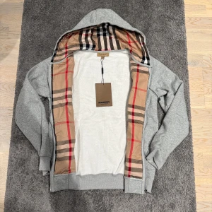 Grå burberry zip hoodie - Skön burberry zip hoodie i nyskick, utan tags. Perfekt nu till vintern. Väldigt varm och fin