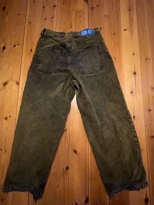 Big Boy baggy jeans XS  - Säljer ett par mörkgröna baggy jeans från Big Boy i storlek XS. Jeansen har bred passform, två stora bakfickor och ett broderat motiv på fickan. Materialet är slitstarkt denim och benen har rå, fransig kant för en edgy look.