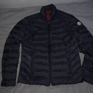 Svart Moncler jacka herr - Snygg svart jacka från Moncler med quiltad design och två dragkedjeförsedda fickor. Jackan har lång ärm, hög krage och röd insida med Moncler-logga. Perfekt för dig som vill ha en stilren och varm jacka med exklusiv känsla. Duger ej pris förhandla🤝