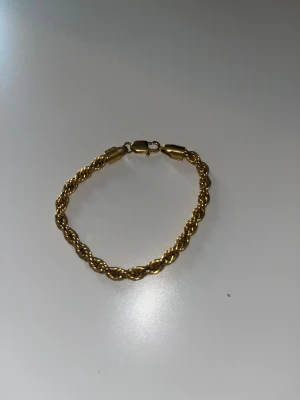 Guldigt tvinnat armband - Snyggt armband i guldton med tvinnad kedja och klassisk låsning. Perfekt för dig som gillar stilrena detaljer och vill ha något som sticker ut lite extra. Armbandet har en rund form och glänsande finish som ger en lyxig vibe.