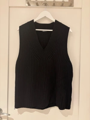 Svart stickad väst från Gina Tricot - Svart, chunky stickad väst från Gina Tricot med bred v-ringning och ribbad struktur. Perfekt att slänga över en skjorta eller t-shirt för en trendig lager-på-lager-look. Modellen är rak och något loose i passformen.