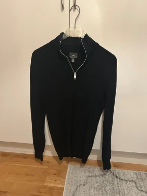 Svart stickad half zip-tröja H&M - Svart stickad tröja från H&M med half zip-dragkedja i halsen. Tröjan har lång ärm och en stilren, enkel design som passar perfekt till jeans eller chinos. Materialet är mjukt och håller dig varm under kyliga dagar.