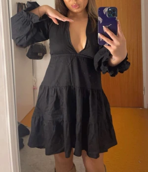 Svart kort klänning med volangärm - Supersnygg svart kort klänning med djup v-ringning,  långa ärmar och volangdetaljer. Klänningen har öppen rygg med knytbar och justerbar rygg, så man kan få klänningen bli tightare vid överkroppen (jag brukar bära storlek 36-38 på klänningar). Ny utan prislapp! Perfekt inför nyår & jul!💕