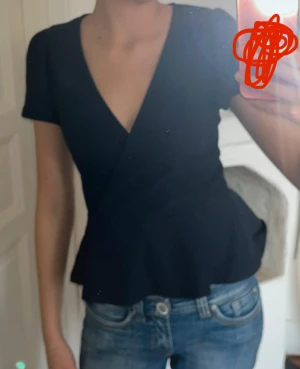 Mörkblå omlottopp med v-ringning - Säljer en mörkblå omlottopp med v-ringad hals och korta ärmar. Toppen har en figurnära passform upptill och faller ut lätt vid midjan. Perfekt att styla med jeans eller kjol för en snygg look.