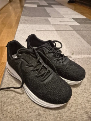 Svarta sneakers med vit sula - Snygga svarta sneakers med vit platt sula och rund tå. Ovandelen är gjord i mesh och syntetmaterial för bra andningsförmåga och komfort. Skorna har klassisk snörning och passar perfekt för dig som gillar en sportig stil.
