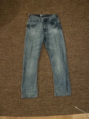 Lee jeans ljusblå jeans straight fit - Säljer ett par klassiska Lee jeans i ljusblå tvätt med raka ben och fem fickor. Jeansen har normal passform och är tillverkade i slitstarkt bomullsjeansmaterial. Perfekt för dig som gillar tidlös denimstil och vill ha ett par jeans som funkar till allt.