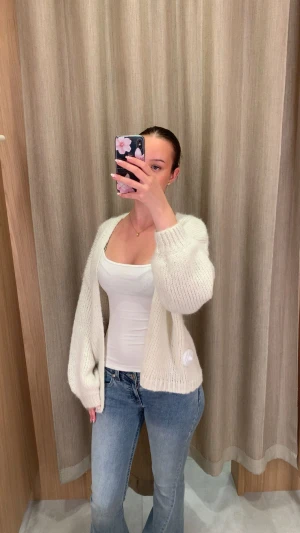 Vit stickad kofta med öppen front - Säljer en mysig vit stickad väst med öppen front och breda ärmhål. Västen har en mjuk och fluffig känsla, ribbade kanter och en avslappnad passform som ger en chill vibe. Perfekt att slänga över en topp för en enkel och snygg look.