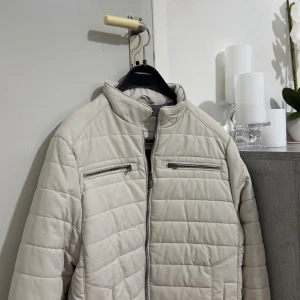 Quiltad pufferjacka LC Waikiki - Säljer en beige pufferjacka från LC Waikiki i storlek S. Jackan har quiltad design, två bröstfickor med dragkedja och en hög krage. Materialet är syntet och jackan stängs med dragkedja framtill. Perfekt för dig som gillar stilren och clean look.
