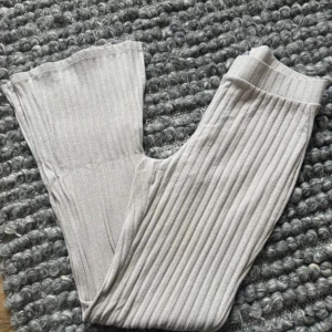 Beige ribbade byxor från Gina Tricot - Säljer ett par beige ribbade byxor från Gina Tricot i storlek S. Byxorna har hög midja, utsvängda ben och slits vid benslutet. Mjukt material som är skönt att ha på sig och ger en chill vibe. Perfekta för dig som gillar trendiga och bekväma plagg.