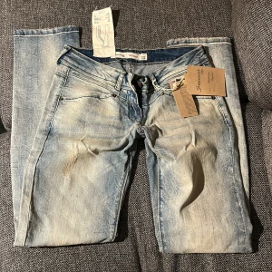 Lågmidjade jeans - Säljer ett par ljusblå Lågmidjade jeans från Jeanswear 72D med snyggt slitna detaljer. Modellen är Regular med raka ben och låg midja. Jeansen har dragkedja och knapp framtill samt coola sömmar på bakfickorna. Midjan är W28 och passar mig som är typ 165
