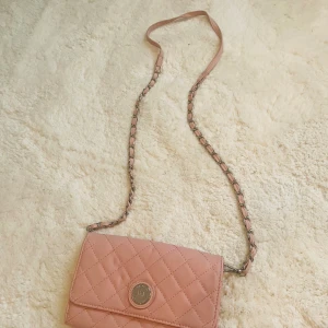 Rosa quiltad axelväska från Don Donna - Supersöt rosa axelväska från Don Donna i quiltad design med silverfärgad kedja och läderdetaljer. Väskan har flera fack, dragkedja inuti och ett snyggt metallmärke framtill. Perfekt storlek för det viktigaste och ger en chic touch till din outfit.