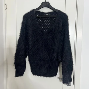 Svart fluffig tröja med v-ringning - Svart fluffig tröja från Bik Bok med v-ringad hals och långärmade ärmar. Materialet är en mix av nylon, bomull och akryl som ger en mjuk och lite lurvig känsla. Perfekt för dig som gillar en cozy och chill stil. Tröjan har ett diskret hålmönster och ribbad nederkant.