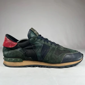 Valentino Rockrunner sneakers camo - Snygga Valentino Rockrunner sneakers i mörkgrön camo med svarta och röda detaljer. Skorna har ovandel i mocka och skinn, klassisk snörning och coola nitar på hälen. Perfekta för dig som vill sticka ut med exklusiva och trendiga sneakers. Skorna kommer utan dustbag och låda. Skorna sitter nästan en storlek större! 🙌 Ställ gärna frågor om det skulle vara något! 🔥😃