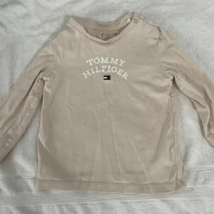 Beige långärmad tröja Tommy Hilfiger - Snygg beige långärmad tröja från Tommy Hilfiger med vit logotyp och klassisk Hilfiger-flagga på bröstet. 