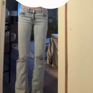 Ljusblå Nelly jeans med hål - Säljer ett par ljusblå Levis jeans med snygga slitningar vid knäna och klassisk femficksdesign. Jeansen har raka ben med lätt bootcut och låg midja. Materialet är mjukt denim och bakfickorna har den ikoniska röda Levis-detaljen.