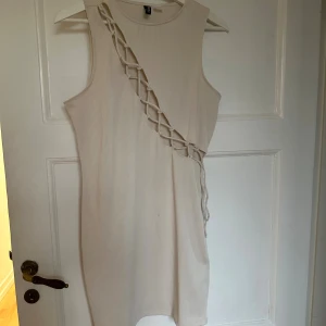 Beige ribbad kortklänning med snörning - Säljer en beige ribbad kortklänning från H&M med unik snörningsdetalj diagonalt över framsidan. Klänningen är ärmlös och har en tight passform som framhäver figuren. Perfekt för dig som vill sticka ut med en cool och trendig look.
