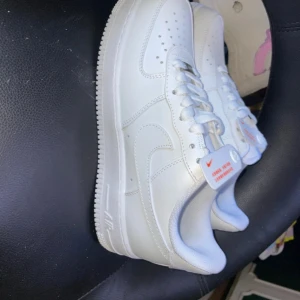 Nike Air Force 1 vita sneakers - Fräscha vita Nike Air Force 1 sneakers med klassisk låg siluett och rund tå. Skorna har snörning, perforerad tåbox och tydlig Nike-logga på sidan och hälen. Tillverkade i slätt skinn med platt sula för en clean och tidlös look.