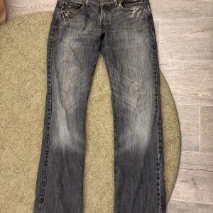 Grå jeans från Jack & Jones - Säljer ett par grå jeans från Jack & Jones med snyggt slitna detaljer och kontrastsömmar. Modellen har klassisk femficksdesign, rak passform och vintage tvätt. Perfekt för dig som gillar en avslappnad stil med lite edge. (Tvättas innan de postas)