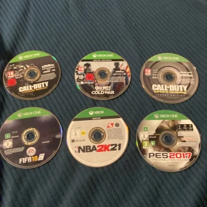 Xbox One Spelpaket (6 spel) - Paket med 6 Xbox One-spel: Call of Duty Advanced Warfare, Cold War, Infinite Warfare, FIFA 18, NBA 2K21 och PES 2017. Skivorna ser ut att vara i gott skick, fodral medföljer. Perfekt för sport- och actionälskare!