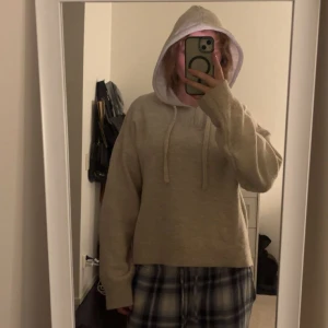 Beige stickad hoodie med huva - Mysig beige stickad hoodie med huva och snörning. Tröjan har lång ärm och en relaxed passform, perfekt för kyliga dagar. Enkel och stilren design utan tryck eller mönster, passar dig som gillar en clean look.