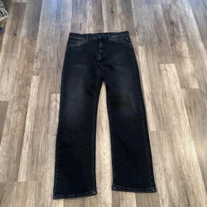 Svarta jeans från Replay straight fit - Säljer ett par svarta jeans från Replay med klassisk femficksdesign och raka ben. Jeansen har en mörk tvätt och tydliga sömmar, samt Replay-logga på fickan och insidan av linningen. Perfekt för dig som gillar stilrena och tidlösa jeans.