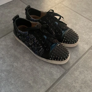 Sällsynta loubs - Unika svarta sneakers med coola silverfärgade nitar på tån och snörning. Sidorna har ett blått och svart abstrakt mönster med glansiga detaljer. Skorna har vit platt sula och rund tå, perfekt för dig som vill sticka ut med din stil, säljs inte mer (de är limited edition) 