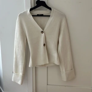 Beige kofta från Gina Tricot XS - Stilren beige kofta från Gina Tricot i storlek XS. Koftan har v-ringning, två knappar framtill och snygga uppvikta ärmslut med dekorativa knappar. Perfekt för lager-på-lager och enkel att matcha med allt. Mjuk och skön känsla.