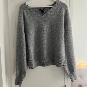 Grå stickad tröja från Lindex - Mysig grå stickad tröja från Lindex med v-ringad hals och ribbade muddar. Perfekt för lite kallare dagar. Långärmad och lite loose fit. Lite nopprig.