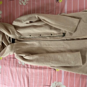 Beige kappa från Vero Moda - Säljer en stilren beige kappa från Vero Moda med lång ärm och snygg krage. Jackan har dragkedja och knappar framtill samt två diskreta fickor på sidorna. Materialet är mjukt och känns lyxigt, perfekt för dig som gillar klassisk och clean look.