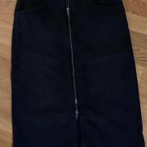 Svart långkjol med dragkedja SoyaConcept - Svart långkjol från SoyaConcept med cool dragkedja framtill och praktiska fickor. Kjolen har en rak passform och är gjord i ett mjukt bomullsmaterial som känns skönt mot huden. Perfekt för dig som gillar stilrena och enkla plagg med en twist.