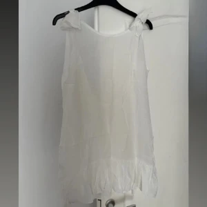 Vit linne klänning  - en söt vit linne - klänningi tunn och luftig bomull. Toppen har knytband på axlarna som man kan knyta själv, en öppen rygg med rosett som man oxå kan knyta själv hur man vill ha den och volangkant nedtill. Fin att ha över bikinin till stranden💕
