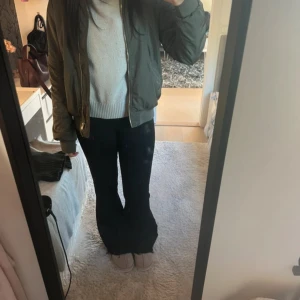 Olivgrön bomberjacka med dragkedja - Säljer en olivgrön bomberjacka med klassisk passform och guldfärgad dragkedja framtill. Jackan har ribbade muddar vid ärmslut och midja samt fickor på sidorna och en ficka med dragkedja på ärmen. Perfekt för dig som gillar streetstyle.