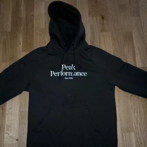 Mörkgrön Peak Performance hoodie helt ny st s - Säljer en mörkgrön hoodie från Peak Performance med vit logga på bröstet. Tröjan har huva med snörning och en stor magficka. Perfekt för dig som gillar en avslappnad och sportig stil.  Storlek smal Använd endast en gång köpt för 1300 ca säljer för 850   jeansen säljes också på första bilden men finns bilder att se.mvh  