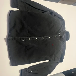 Ralph Lauren skjorta - Svart långärmad skjorta från Polo Ralph Lauren i 100% bomull. Klassisk krage, vita knappar framtill och på ärmslut. Broderad röd Polo-logga på bröstet ger en snygg kontrast. Passar dig som gillar stilrena och tidlösa plagg.