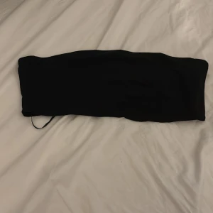 Svart bandeau tubtopp från H&M Divided - Säljer en svart bandeau tubtopp från H&M Divided i storlek L. Toppen är helt ärmlös och har en enkel, stilren design utan mönster eller detaljer. Perfekt för dig som gillar minimalistiska plagg och vill ha en basic topp till garderoben.
