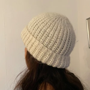 Ribbstickad vit mössa i ull - Snygg ribbstickad mössa i mjuk vit ull. Klassisk form med bred uppvikt kant som ger en chill och tidlös vibe. Perfekt för kalla dagar och enkel att matcha med din vinterstil. Passar dig som gillar enkel och clean look. Passar huvudmått 55cm och större.
