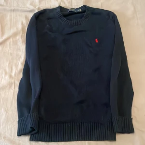 Mörkblå stickad tröja Polo Ralph Lauren - Snygg mörkblå stickad tröja från Polo Ralph Lauren med klassisk röd logga broderad på bröstet.  perfekt för lager-på-lager under kyliga dagar. 
