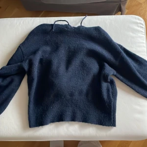 Mörkblå stickad hoodie Gina Tricot - Mysig mörkblå stickad hoodie från Gina Tricot i storlek 158/164. Tröjan har huva med snörning och långa ärmar. Ribbad nederkant och ärmslut ger en skön passform. Perfekt för kyliga dagar när du vill vara både bekväm och snygg.