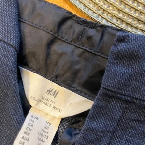 Mörkblå slim fit byxor från H&M - Snygga mörkblå byxor från H&M i slim fit-modell med justerbar midja. Byxorna har raka ben och är tillverkade i ett mjukt material som ger en skön känsla. Perfekta för dig som gillar en stilren och enkel look.