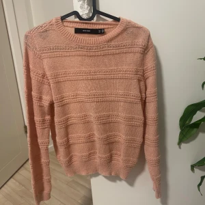 Stickad rosa tröja från Vero Moda - Mysig stickad tröja från Vero Moda i en ljusrosa ton. Tröjan har ett diskret ribbat mönster med horisontella ränder och rund hals. Långärmad och perfekt för kyliga dagar. Passar dig som gillar enkel och stilren design.