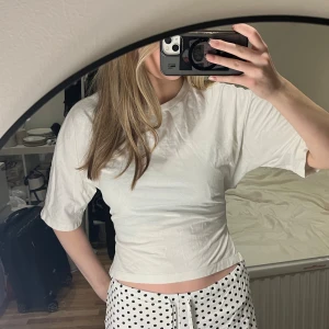 Vit croppad t-shirt med knyt i sidan - Säljer en fräsch vit croppad t-shirt med korta ärmar och snygg knytning i sidan. T-shirten har en enkel och clean look, perfekt för dig som gillar stilrena plagg med en twist. Materialet är mjukt och känns skönt mot huden.