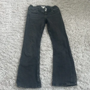 Bootcut jeans från Gina Tricot, svart - Svarta bootcut jeans från Gina Tricot med snygga silverfärgade knappar och klassiska fickor både fram och bak. Jeansen har en lätt tvättad look och är tillverkade i jeansmaterial. Passar dig som gillar en lite vidare siluett nertill.