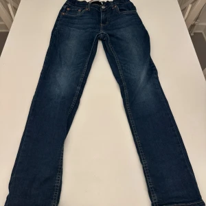 Levi's 512 Slim Tapered jeans blå, BARN - Snygga Levi's 512 Slim Tapered jeans för barn i mörkblå tvätt med klassiska fem fickor och kontrastsömmar. Modellen har smal passform och avsmalnande ben, perfekt för en modern look. Ikonisk Levi's patch och röd etikett på bakfickan. Innerben 66 cm, stl 12A , 152cm