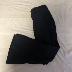 Svarta kostymbyxor från Gina Tricot - Snygga svarta låg midjade kostymbyxor från Gina Tricot i klassisk utsvängd modell med vida ben. Byxorna har hällor för bälte, dold dragkedja och knappstängning fram. Perfekta för dig som gillar stilrena och tidlösa plagg. Materialet är mjukt och har en lätt stretch. Hade gärna visat hur de sitter på men tyvärr är de för små.